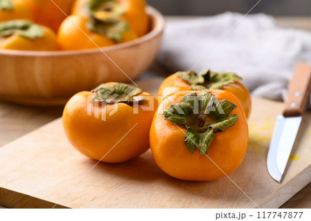 Ripe persimmon fruit on cutting wooden board with knife Ripe persimmon fruit on cutting wooden board with knife 117747877