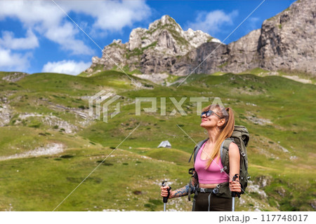 Woman Hiker Walking with Hiking Poles on Mountains 117748017