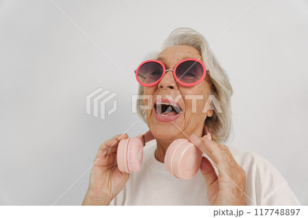 A Joyful Senior Woman Wearing Headphones and Stylish Sunglasses Enjoying Music Outdoors 117748897