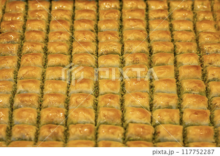 Golden background of of baklava. The flaky layers are filled with pistachios and glazed with syrup Golden background of of baklava. The flaky layers are filled with pistachios and glazed with syrup 117752287