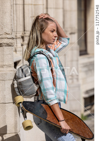 A young woman in a plaid shirt and backpack enjoys skateboarding outdoors in an urban setting A young woman in a plaid shirt and backpack enjoys skateboarding outdoors in an urban setting 117752548