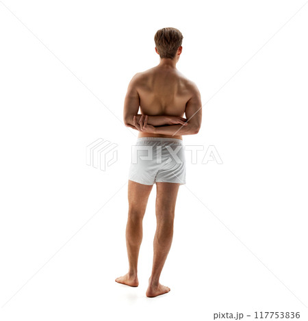 Rear view photo of young man in white underwear posing holding hands behind back against white studio background. Posture. 117753836