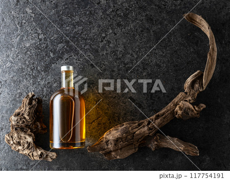 Bottle of whiskey and old snags on a black stone background. 117754191