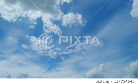 Blue clear sky with white cumulus and cirrus spindrift clouds background. Light white cirrus clouds in blue sky on a summer day. Timelapse. 117754643