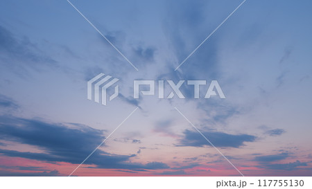 Sun below the horizon and clouds in the fiery dramatic sky. Cirrus clouds illuminated by sunbeams. Timelapse. 117755130