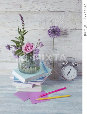 A stack of books, an alarm clock, a bouquet of flowers and stationery materials on a wooden background. Back to school. A stack of books, an alarm clock, a bouquet of flowers and stationery materials on a wooden background. Back to school. 117755857