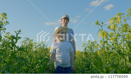 Happy Beauty Woman And Her Little Son Walking In Yellow Rapeseed Field. Happy Child Walking. Love And Family And Joy Concept. Happy Beauty Woman And Her Little Son Walking In Yellow Rapeseed Field. Happy Child Walking. Love And Family And Joy Concept. 117756099