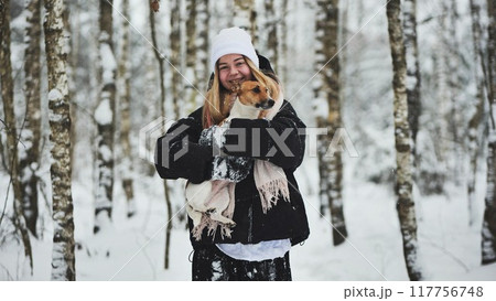 A girl cuddles a Jack Russell Terrier dog in the woods in winter. A girl cuddles a Jack Russell Terrier dog in the woods in winter. 117756748
