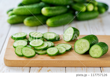 Whole and sliced fresh cucumbers on a cutting board on a wooden table, selective focus. 117757126