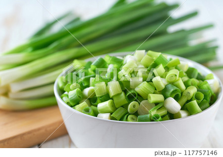 Chopped scallions or young spring onion in a ceramic bowl , on a kitchen table. Chopped scallions or young spring onion in a ceramic bowl , on a kitchen table. 117757146
