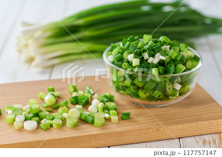 Chopped scallions or young spring onion in a clear glass , on a kitchen table. 117757147