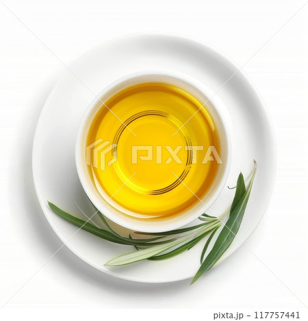 A small, white saucer filled with a pool of emerald green olive oil. A single, green olive leaf rests on the oil's surface. The saucer sits on a clean white background. A small, white saucer filled with a pool of emerald green olive oil. A single, green olive leaf rests on the oil's surface. The saucer sits on a clean white background. 117757441