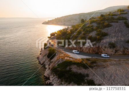 Scenic coastal road travels along the waterfront at sunset in a beautiful mountainous region.  117758531
