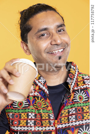 Portrait of ecstatic man wearing traditional indian clothes sipping fresh coffee to wake up and be energized. Merry person with colorful vest drinking hot beverage, studio background, close up shot Portrait of ecstatic man wearing traditional indian clothes sipping fresh coffee to wake up and be energized. Merry person with colorful vest drinking hot beverage, studio background, close up shot 117758792
