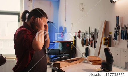 Manufacturer putting safety goggles on while selecting quality wood materials meeting client commission requirements. Woodworking expert doing quality assurance on timber block, camera B 117758822