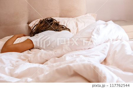Person with dreadlocks sleeping on bed in bright bedroom. Person with dreadlocks sleeping on bed in bright bedroom. 117762544