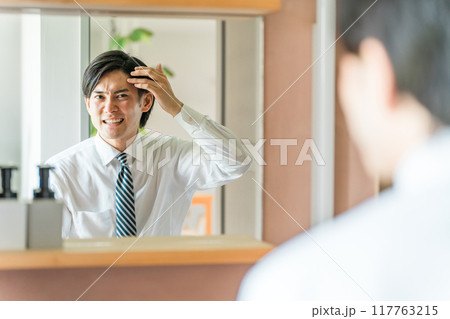 洗面所で頭皮の生え際を機にする若いアジア人男性（薄毛・脱毛・AGA・抜け毛） 117763215