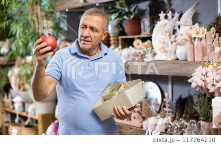 Mature man is preparing for Christmas and choosing balls Mature man is preparing for Christmas and choosing balls 117764210