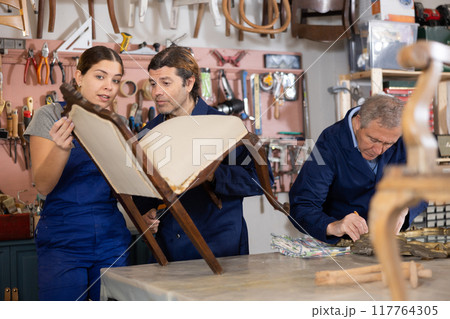 Portrait of three woodworkers restorers renovating Victorian chair and mirror frame in workshop Portrait of three woodworkers restorers renovating Victorian chair and mirror frame in workshop 117764305
