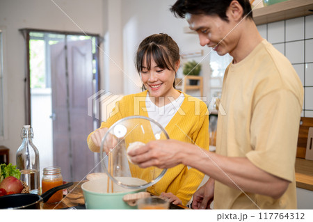 A lovely young Asian couple is enjoying making noodles together in the kitchen. A lovely young Asian couple is enjoying making noodles together in the kitchen. 117764312