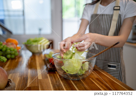 A close-up image of a woman preparing a salad bowl at the kitchen table, making healthy food at home A close-up image of a woman preparing a salad bowl at the kitchen table, making healthy food at home 117764352