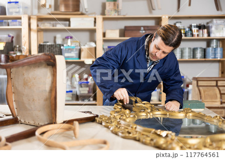 collected male restorer carefully covers carved wooden frame of antique mirror with layer of varnish 117764561