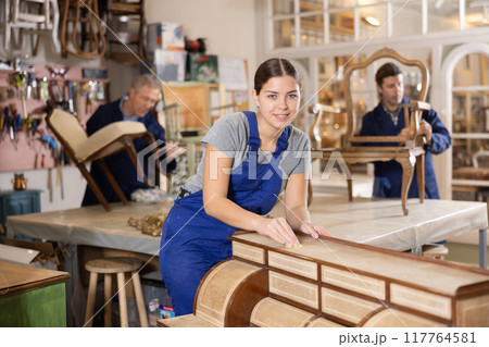 Woman restorer carefully and carefully restores chest of drawers in restoration workshop Woman restorer carefully and carefully restores chest of drawers in restoration workshop 117764581