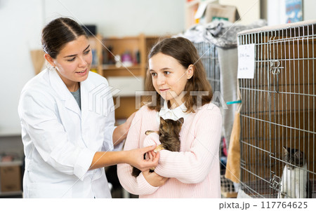 Tween girl standing with female shelter worker, holding kitten 117764625