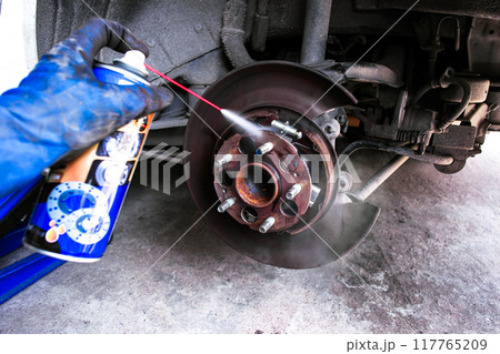 A mechanic cleans the inside of a car brake drum with cleaning spray 117765209
