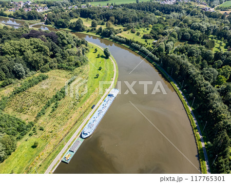 Aerial view shows a calm river with a barge drifting gracefully through its waters Aerial view shows a calm river with a barge drifting gracefully through its waters 117765301