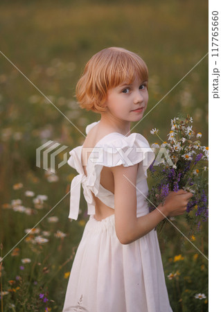 A young girl is standing in a field of flowers, holding a bouquet of flowers 117765660