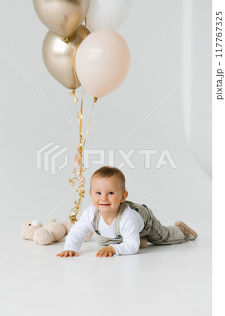 Smiling happy birthday baby crawling on the floor against the background of balloons Smiling happy birthday baby crawling on the floor against the background of balloons 117767325