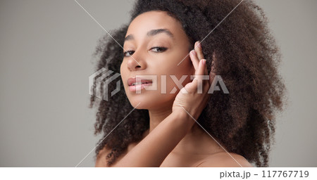 Beauty and healthcare - beautiful African American woman with curly afro hairstyle and clean, healthy skin touching her face, neck, shoulders, looking at the camera with a calm look and a slight smile Beauty and healthcare - beautiful African American woman with curly afro hairstyle and clean, healthy skin touching her face, neck, shoulders, looking at the camera with a calm look and a slight smile 117767719