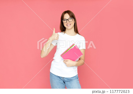 An attractive, young girl in glasses and books in her hands 117772023