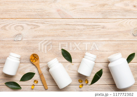 Omega-3 capsules lie in white bottle on a table with green leaves background. Fish oil tablets. Biologically active additives. omega 6, omega 9, vitamin A, E, D, vitamin D3 top view with copy space 117772302