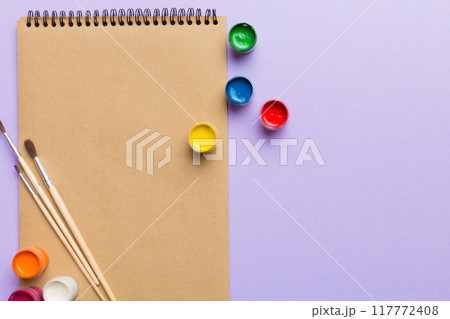 Album pages and paints, pencils, brush on a colored background. Top view with empty space. workplace for creativity. home teaching concept drawing 117772408