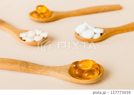 Vitamin capsules in a spoon on a colored background. Pills served as a healthy meal. Red soft gel vitamin supplement capsules on spoon 117773039