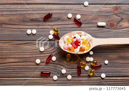 Vitamin capsules in a spoon on a colored background. Pills served as a healthy meal. Red soft gel vitamin supplement capsules on spoon Vitamin capsules in a spoon on a colored background. Pills served as a healthy meal. Red soft gel vitamin supplement capsules on spoon 117773045