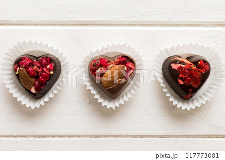 chocolate sweets in the form of a heart with fruits and nuts on a colored background. top view with space for text, holiday concept chocolate sweets in the form of a heart with fruits and nuts on a colored background. top view with space for text, holiday concept 117773081