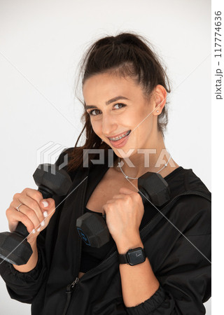 Young girl posing with dumbbells for power training, indoors. athlete wearing black leggings and shirt Young girl posing with dumbbells for power training, indoors. athlete wearing black leggings and shirt 117774636