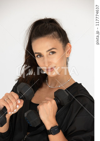 Young girl posing with dumbbells for power training, indoors. athlete wearing black leggings and shirt Young girl posing with dumbbells for power training, indoors. athlete wearing black leggings and shirt 117774637