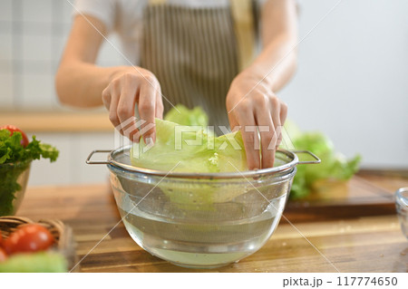 Close up shot of woman washing lettuce while preparing healthy vegan salad in kitchen 117774650