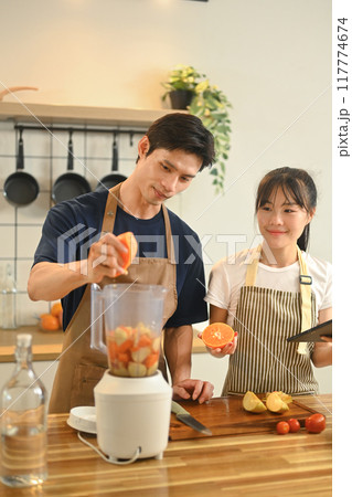 Young couple making healthy smoothie with a colorful mix of fruits in their modern kitchen 117774674