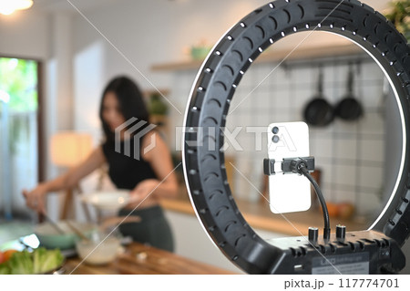 Smartphone and ring lamp for blogging and recording video, athletic woman recording video about healthy food and cooking 117774701