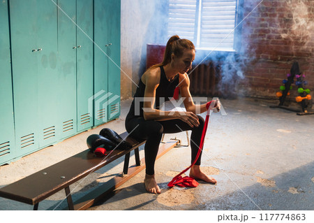 Women self defense girl power. Woman fighter preparing for fight wrapping hands with red boxing wraps sports protective bandages. Strong girl ready for fight active exercise sparring workout training 117774863