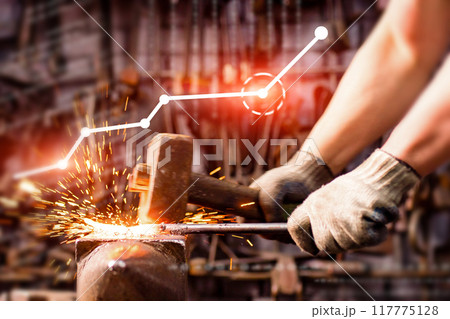 A person is hammering a piece of metal in front of a graph that shows a downward A person is hammering a piece of metal in front of a graph that shows a downward 117775128