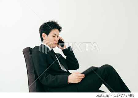 椅子に座ってスマートフォンを使う20代の若い男性 117775499