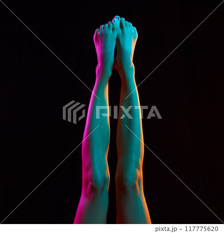 Female, barefoot slim legs in vibrant, colorful neon light against black background. Epilation and anti-cellulite massage. Female, barefoot slim legs in vibrant, colorful neon light against black background. Epilation and anti-cellulite massage. 117775620
