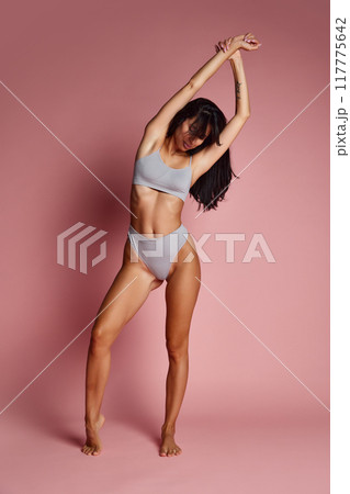 Full length photo of young athletic woman posing raising hands against pink studio background. Fit, slim model. Full length photo of young athletic woman posing raising hands against pink studio background. Fit, slim model. 117775642