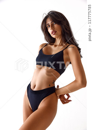 Woman gazing ahead, showcasing her long hair and sleek black lingerie, highlighting her natural beauty against white studio background. Woman gazing ahead, showcasing her long hair and sleek black lingerie, highlighting her natural beauty against white studio background. 117775785